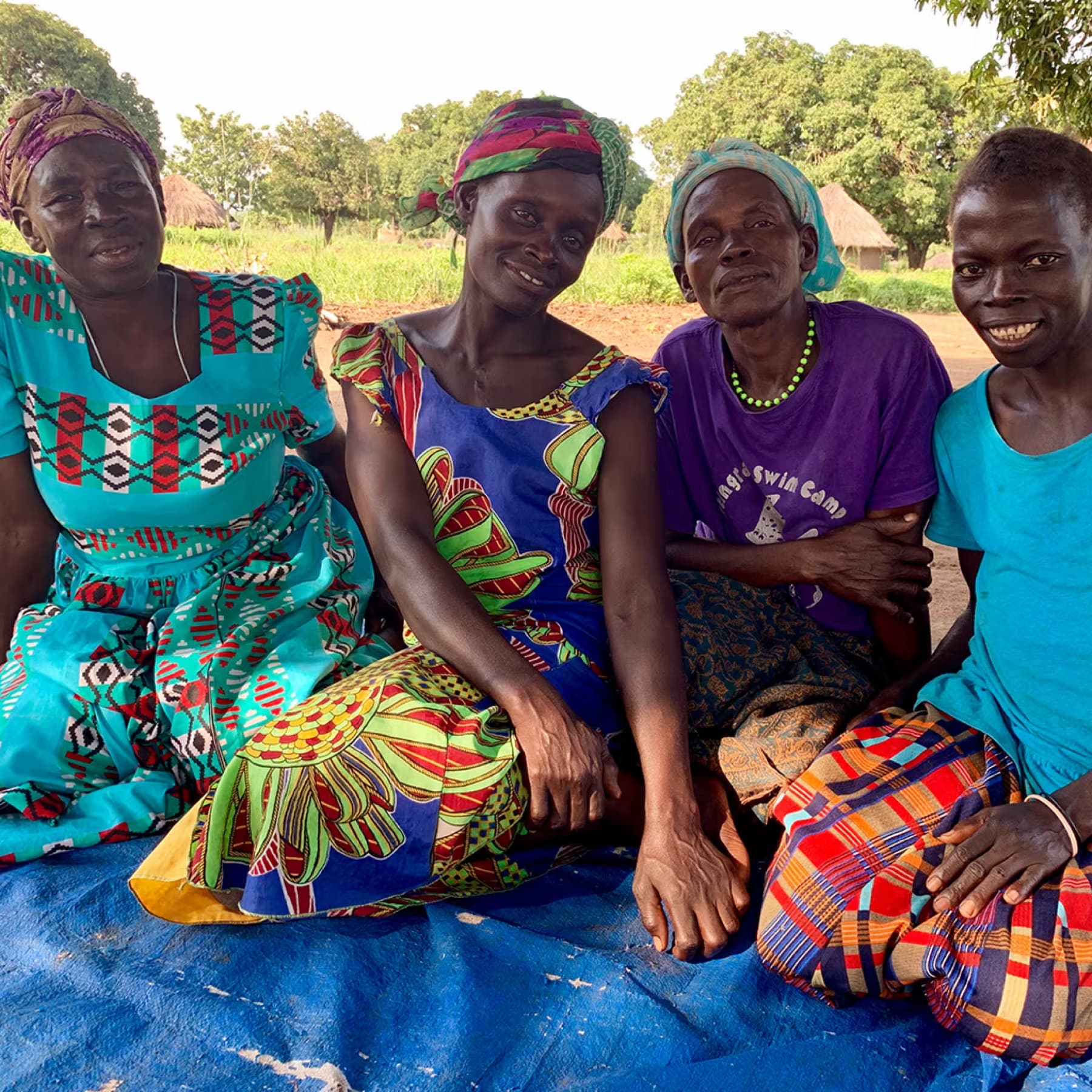 Traditional midwives from the Atiak collective seated together in bright kitenge, laughing