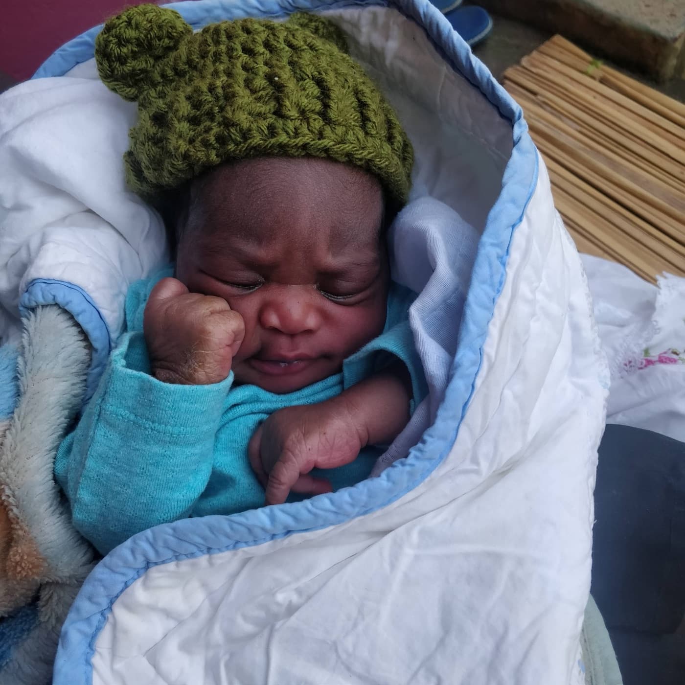 A newborn in a knitted hat wrapped in a blue blanket
